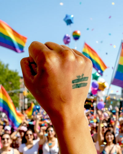 Raised fist at a summer Pride parade, FREEBRD tattoo visible, rainbow flags and crowd in background, Unity blog series.