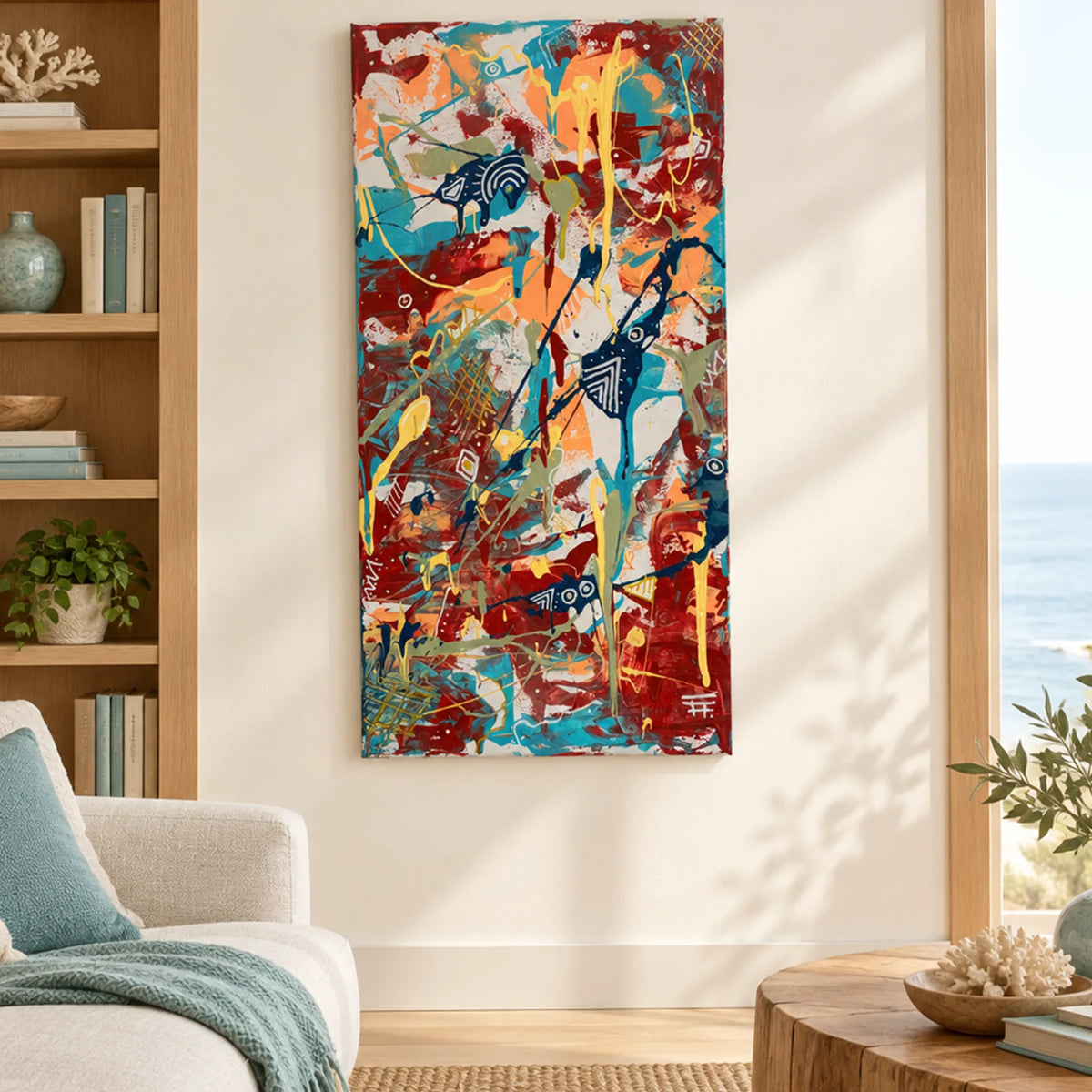 Seaside Mantra abstract artwork with turquoise, red, peach, and yellow splashes, displayed vertically beside a wooden bookshelf in a sunlit coastal living room.