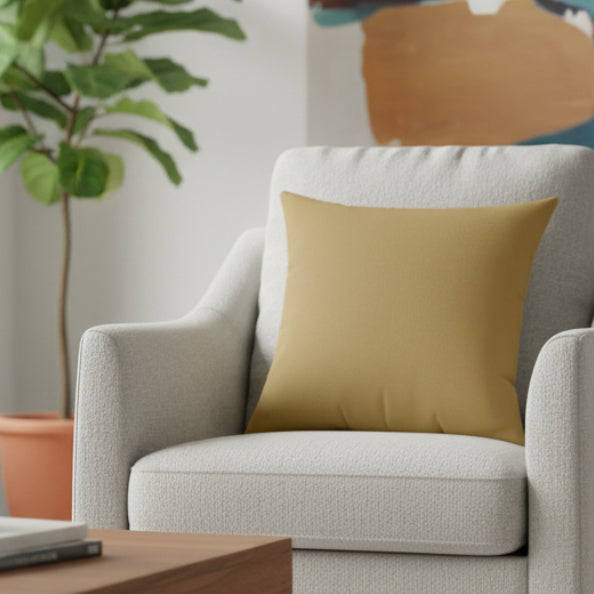 Ash Mustard Faux Suede Square Pillow in a sofa chair with a plant in the background.