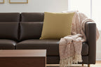Gray sofa with an ash Mustard faux suede pillow and a knitted blanket in a living room setting.