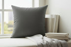 Atomic Gray Faux Suede pillow on a white surface with books and a blanket in the background