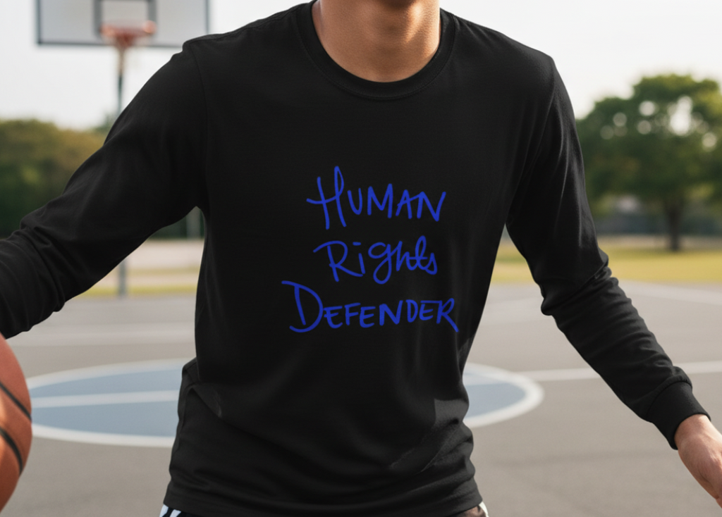 Person wearing a Freebrd designed black long-sleeve shirt with 'Human Rights Defender' text on a basketball court.