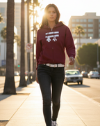Person wearing a maroon hoodie with a Freebrd logo, walking on a sidewalk with palm trees and buildings in the background.