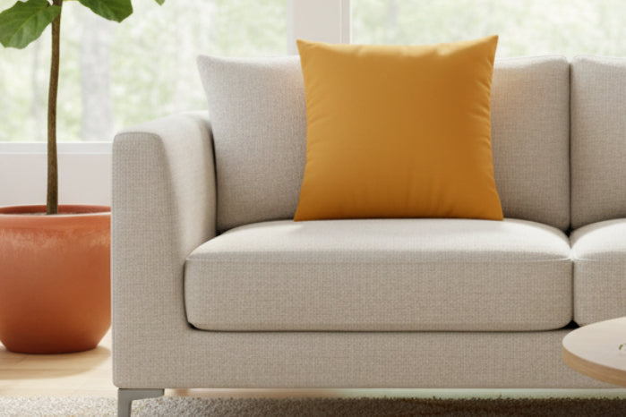 Beige sofa with a Dixie Florida orange faux suede pillow in a bright living room setting