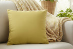 Dull Gold Yellow Faux Suede Square Pillow alongside Decorative pillows on a beige sofa with a bright, sunlit room in the background