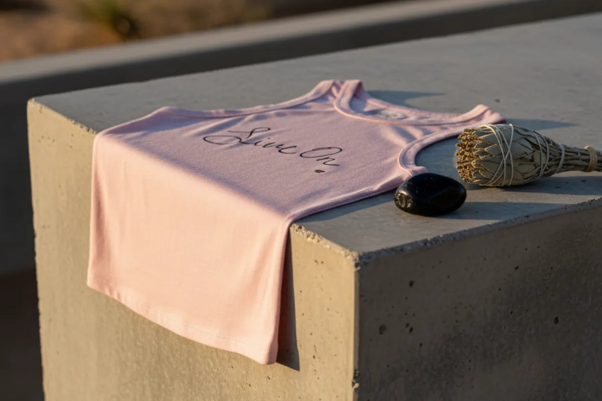 Pink tank top with 'Live on' text on a concrete surface with a black obsidian stone and dried sage plant.