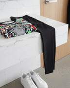 Colorful folded Freebrd abstract "Zonch" apparel, black pants, and white sneakers on a white bench.