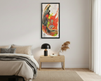 A bedroom lifestyle view of the “Grid Riser Rhino” Abstract Framed Art by FREEBRD on a 1.25” canvas with a 16" x 32” Vertical frame, showcasing vibrant orange, red, green and black acrylic textures with hints of vivid yellow, coral and gold, framed in an espresso wood FSC certified frame hanging above a wooden nightstand with a lamp and accent decor. 