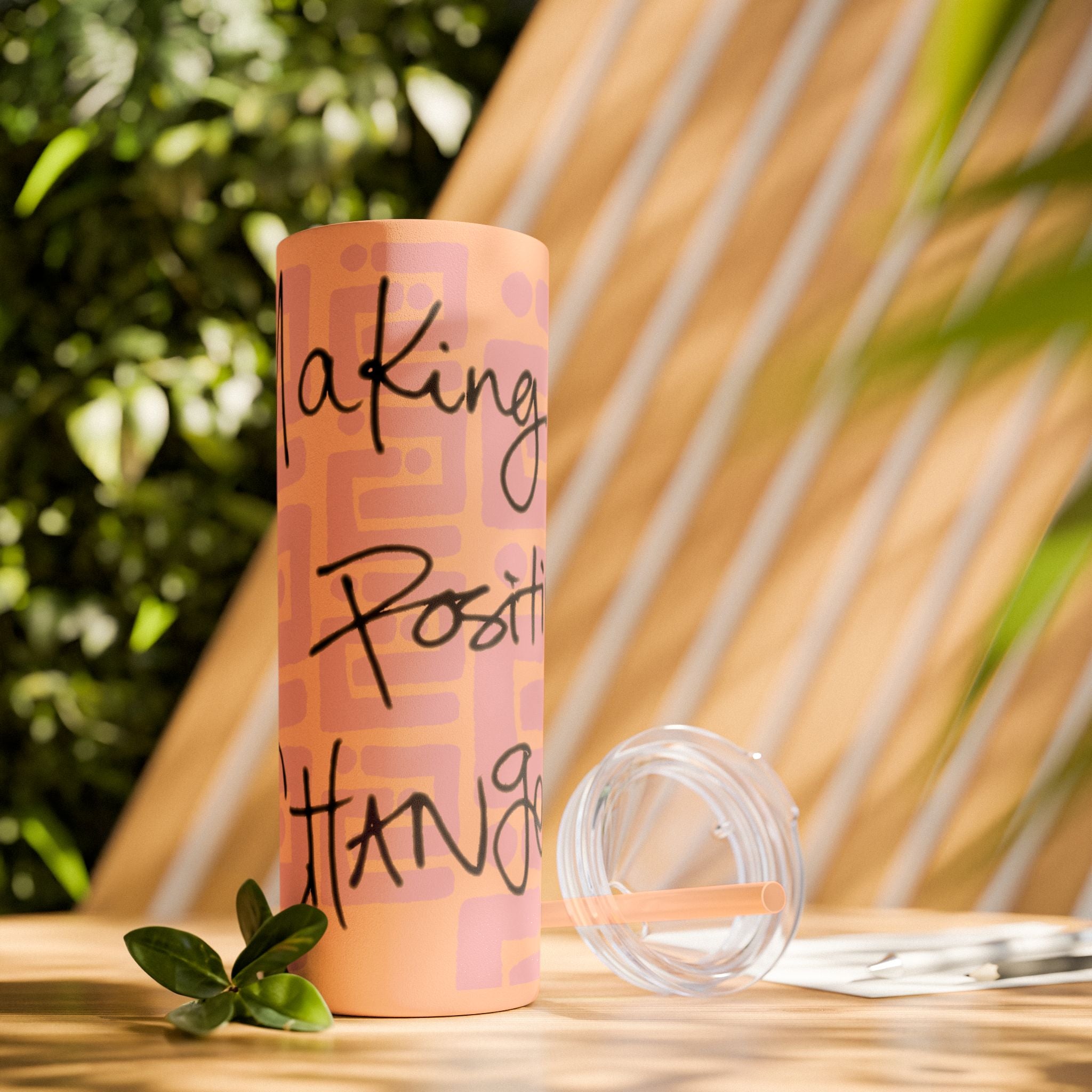 Matte blush tumbler with motivational text on a wooden surface with plants in the background