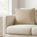 Natural Jute Faux Suede Square Pillow on a beige sofa in a bright room with light streaming through a window.