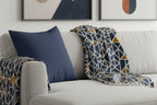 Gray sofa with Rugged Blue Faux Suede Pillow and patterned blanket against a wall with abstract art.