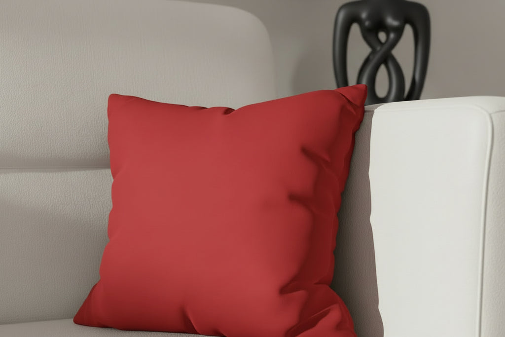 Red pillow on a beige sofa with a blurred black sculpture in the background