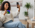 Woman sitting on a couch holding a smartphone and a Freebrd rainbow wave mug in a living room.