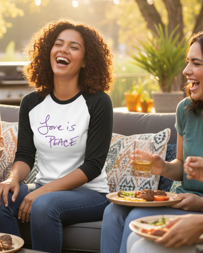 Group of women sitting outdoors, enjoying a meal and drinks, with one wearing a Freebrd 'Love is Peace' shirt.