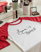 White Freebrd raglan t-shirt with red sleeves and 'Love is Peace' text on a vanity table with makeup.