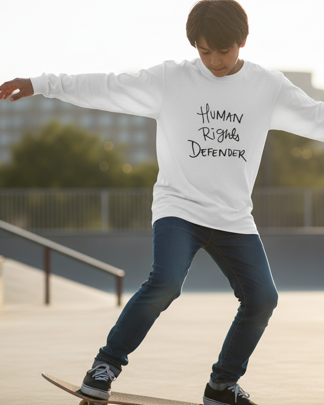 Young person skateboarding at a park wearing a Freebrd designed white long sleeve with 'Human Rights Defender' text
