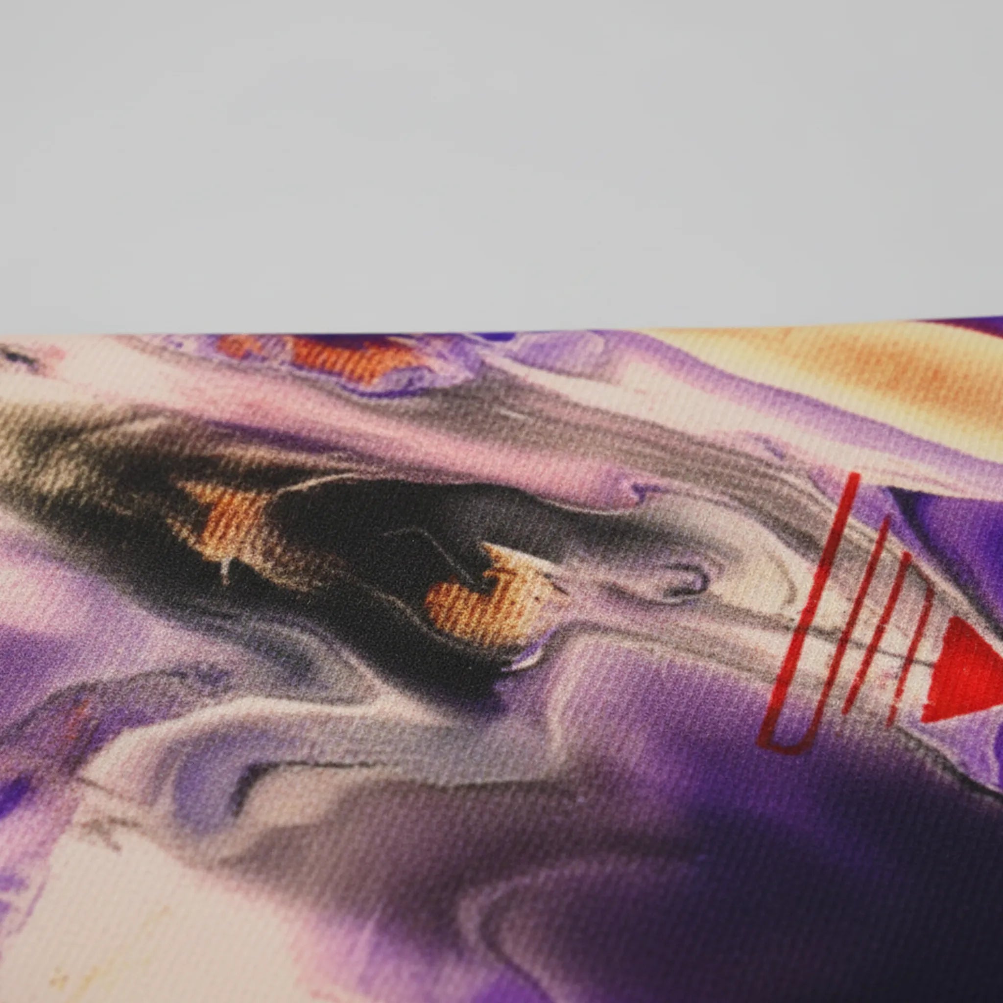 All-over print tee, close-up texture showing polyester fabric weave and abstract art print featuring purple fluid pour, yellow hand motif, red energy strokes, and tribal geometric patterns.