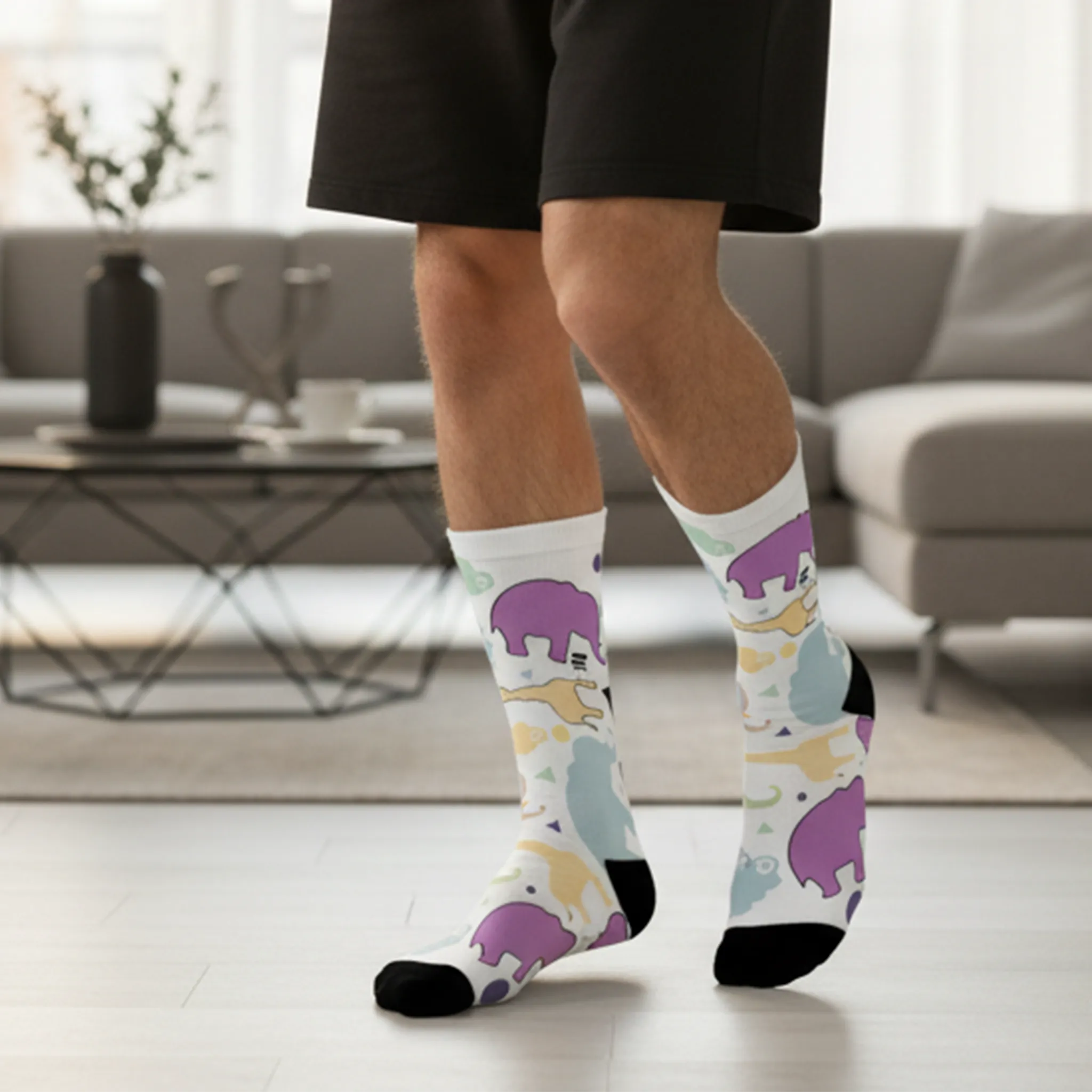 Animal Clouds Cushioned Mid-calf Socks. Featuring vibrant giraffe and elephant cloud prints in playful sea green, purple, and yellow colors with a black toe and heel being worn by a man.