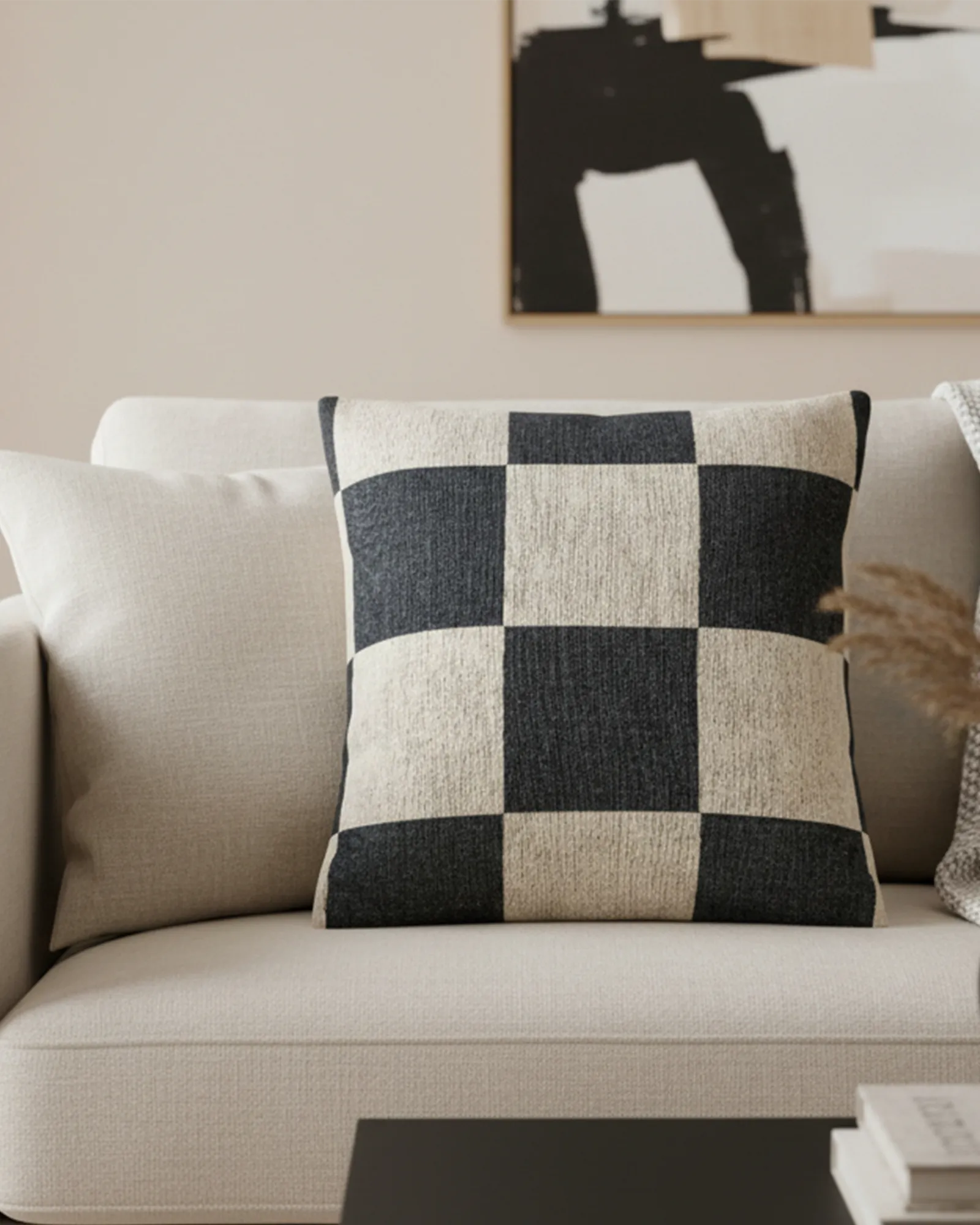 A preview of the Atomic Grey Woven Checkered Decorative Pillow showing dark grey checker squares on an ivory oatmeal background on a  neutral couch with art on the wall in the background.