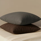 Atomic Grey and Saddle Brown 18x18 faux suede throw pillows stacked on cream linen bedding, size reference.