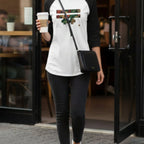A woman wearing the Autumn Floral Freebrd Raglan with black jeans, walking out of a coffee shop holding a coffee cup, showcasing the botanical floral graphic on the front.