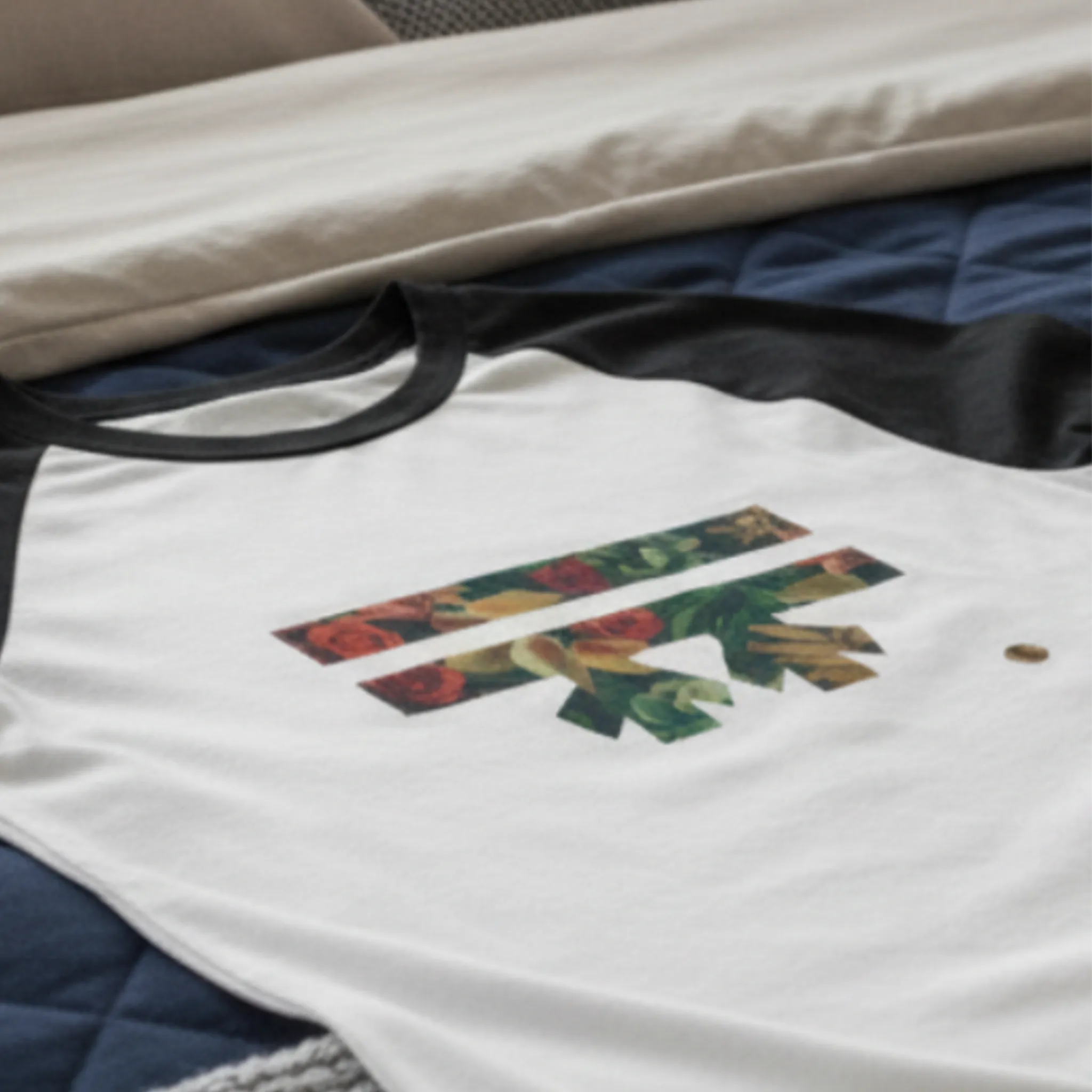 A close-up vignette of the Autumn Floral Freebrd Raglan laid on a bed, highlighting the autumn botanical print detail of red roses, green leaves, and peach gold florals within the FREEBRD logo graphic.