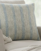 A preview of the Coastal Danish Blue Off White Woven Stripe Pillow showing an ivory background and danish blue pinstripes sitting on a sofa chair. 