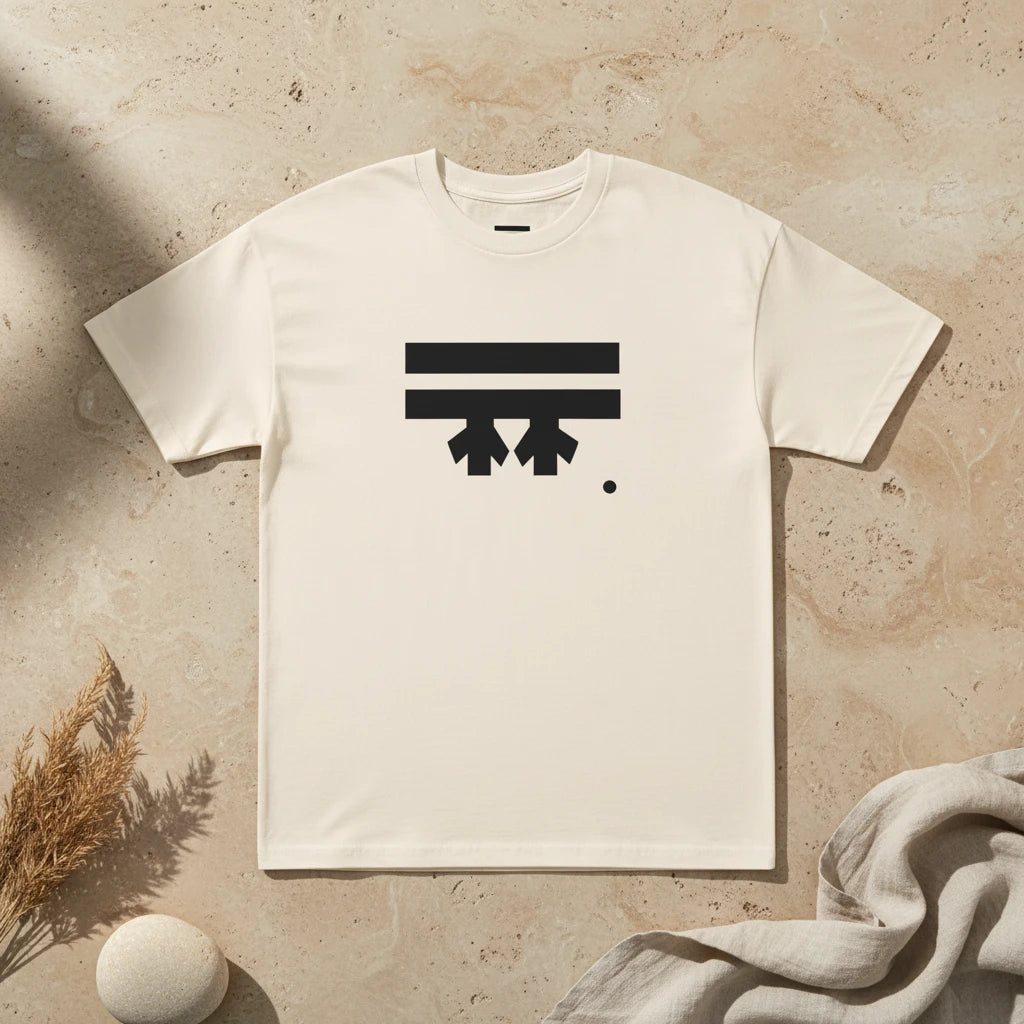 Freebrd Logo Classic T-Shirt in cream, that has a black Freebrd Logo on the chest lying on a tan marble flat surface with a sand stone and dried flowers.