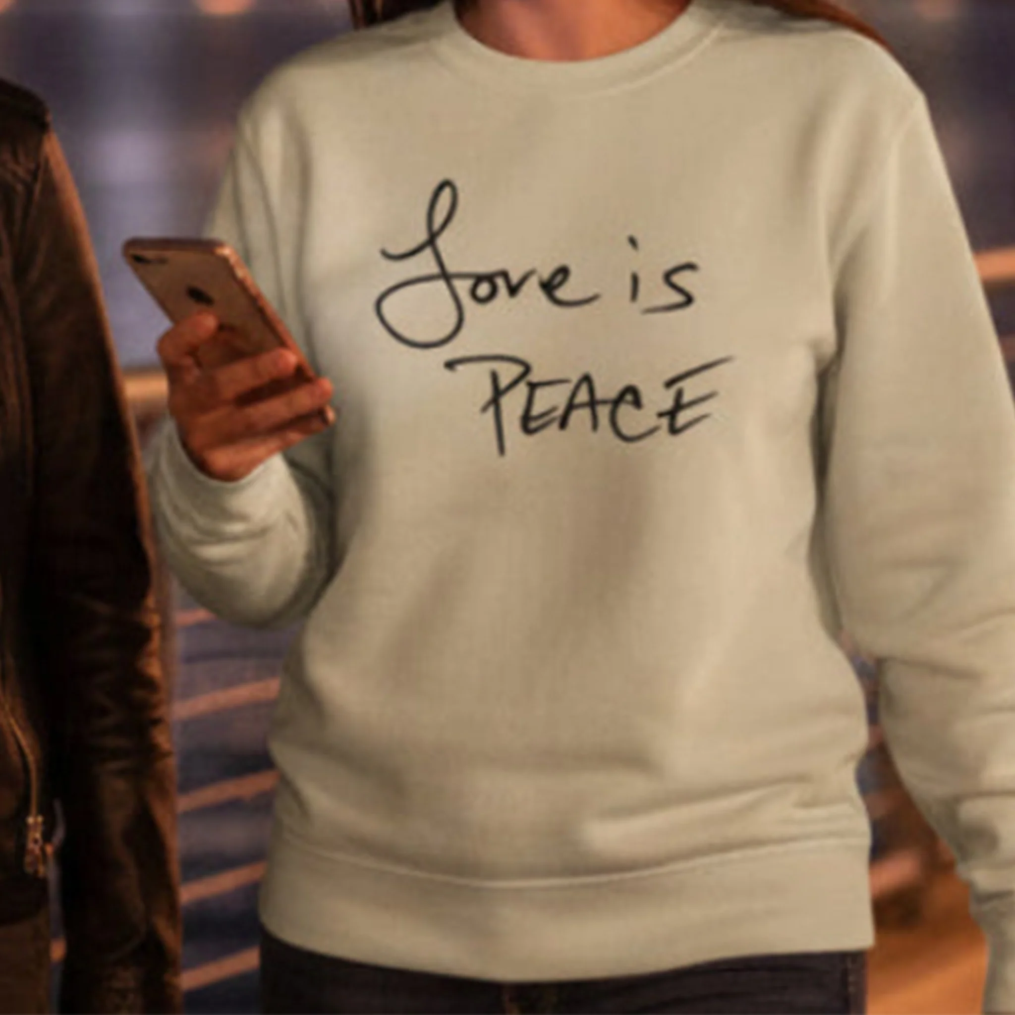 Desert sand Love is Peace crewneck sweatshirt, black print, styled with denim jeans, front view.