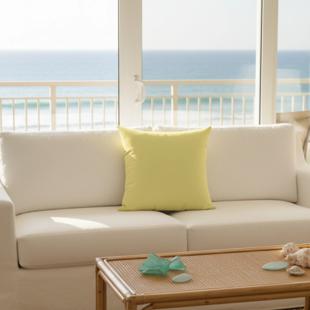 Butter yellow faux suede pillow styled on a couch in a bright coastal living room with sea glass decor.