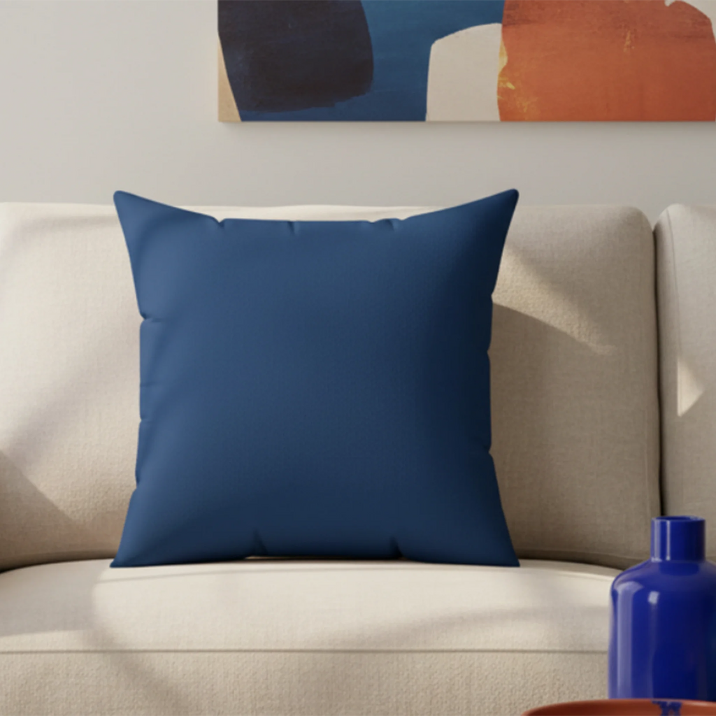 A living room lifestyle preview of the elegant blue faux suede pillow on a cream sofa with abstract navy and terracotta wall art and cobalt blue vase.