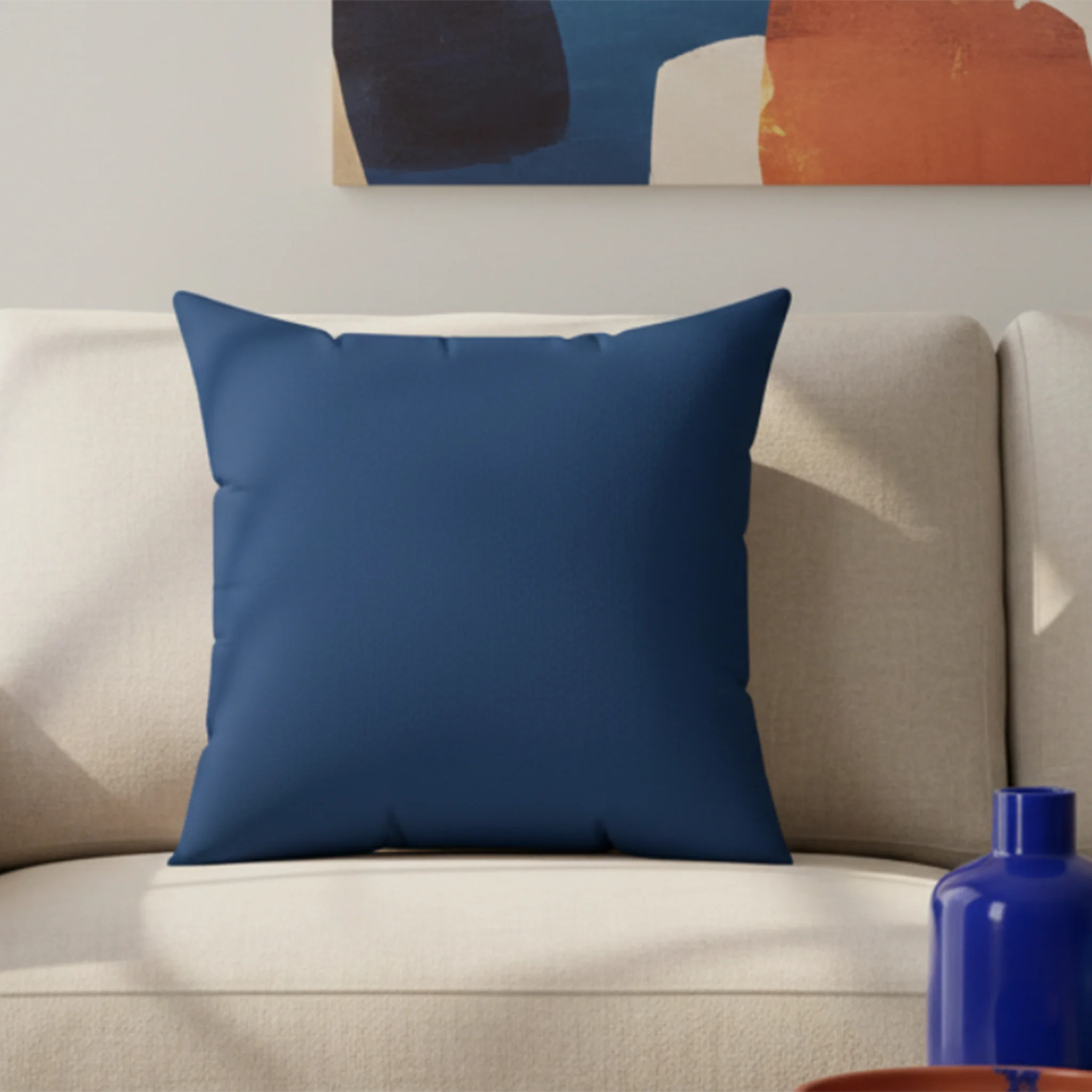 A living room lifestyle preview of the elegant blue faux suede pillow on a cream sofa with abstract navy and terracotta wall art and cobalt blue vase.