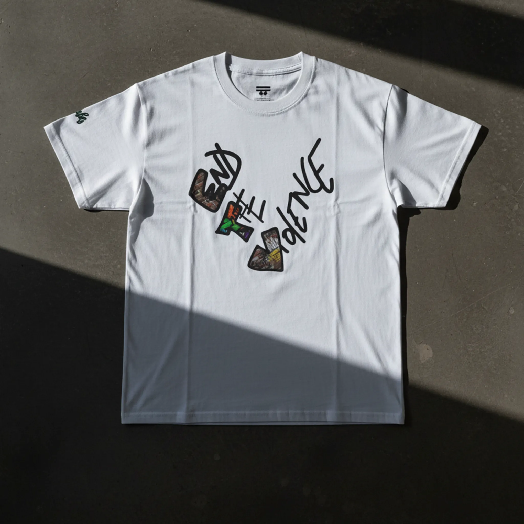 Graphic heart t-shirt with graffiti-style "End the Violence" mixed-media art, white, flat lay on dark concrete surface