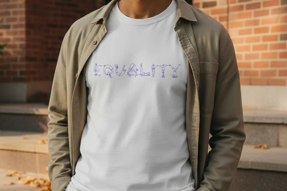 A person wearing a white crew-neck t-shirt with the word 'EQUALITY' spelled out in purple graphic skateboarder art letters across the chest, layered under an open beige overshirt, standing outdoors in front of a brick wall.