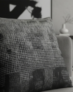 Grey modern sofa in a minimalist living room with black abstract wall art and a white ceramic vase styled with the Faded Geometric Woven Pillow.