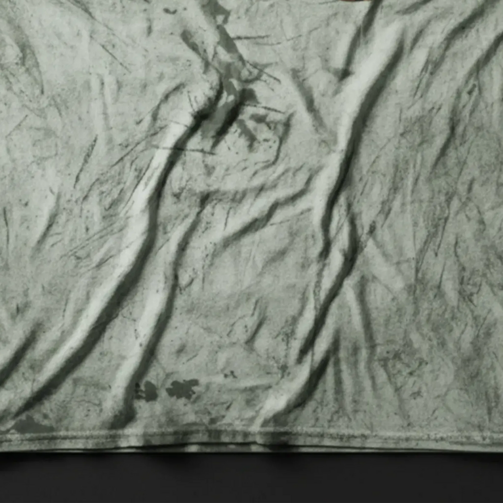 A close-up bird's eye flat lay of the fern cheetah marble tie-dye tee on a dark slate surface, highlighting the garment-dyed wash texture.