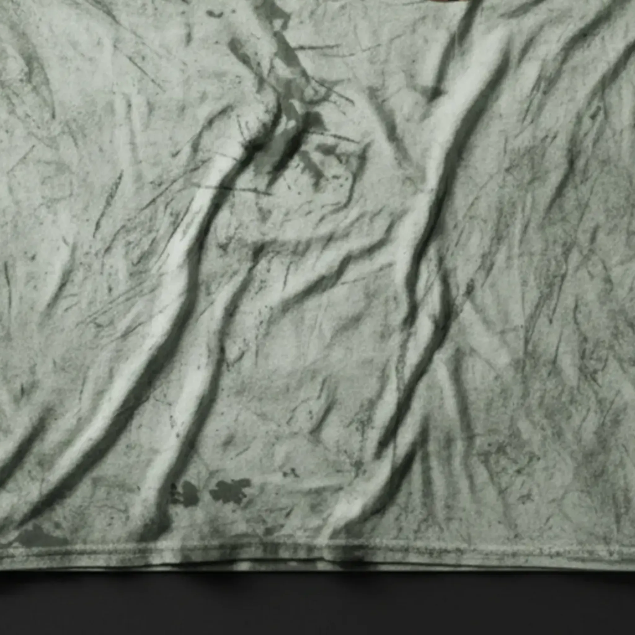 A close-up bird's eye flat lay of the fern cheetah marble tie-dye tee on a dark slate surface, highlighting the garment-dyed wash texture.