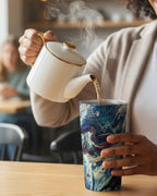 Lady pouring steaming liquid from a white teapot, into the colorful Abstract Stainless Steel Travel Mug 15oz with a marble look displaying navy, white, gold, magenta, black and shades of red, in a casual setting.