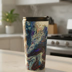 Freebrd Afrostar stainless steel travel mug sitting on a kitchen counter in early morning golden light with steam rising from the abstract acrylic pour design in navy, blue, white and red.