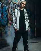 Person wearing an ‘Ecliptic’ Freebrd full-zip hoodie in an urban editorial setting with a graffiti wall backdrop and moody city lighting for a bold bold black-and-white abstract art vibe.