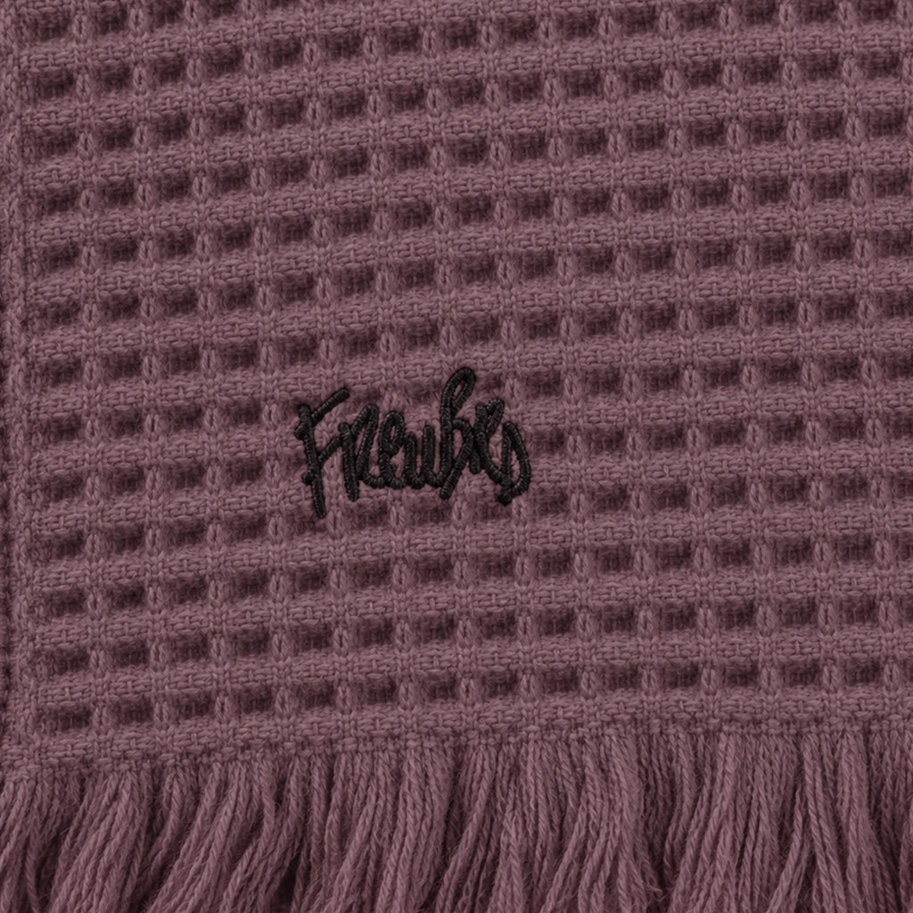 Close-up of a Dusky Orchid waffle throw showing black embroidered lettering above the fringed edge.