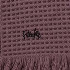 Close-up of a Dusky Orchid waffle throw showing black embroidered lettering above the fringed edge.