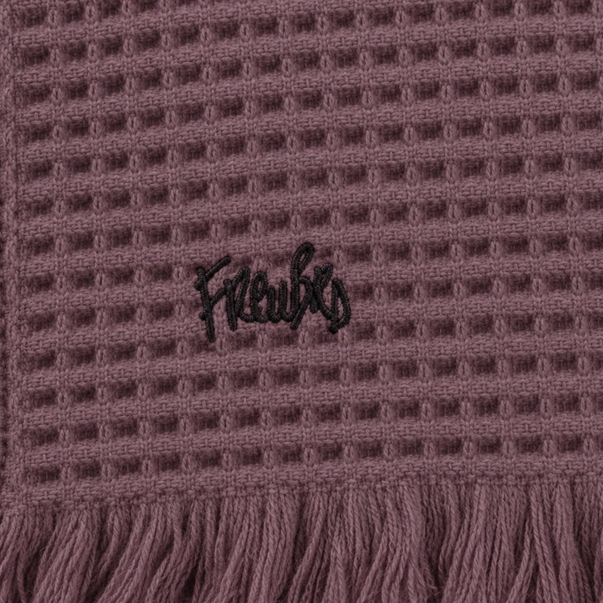 Close-up of a Dusky Orchid waffle throw showing black embroidered lettering above the fringed edge.