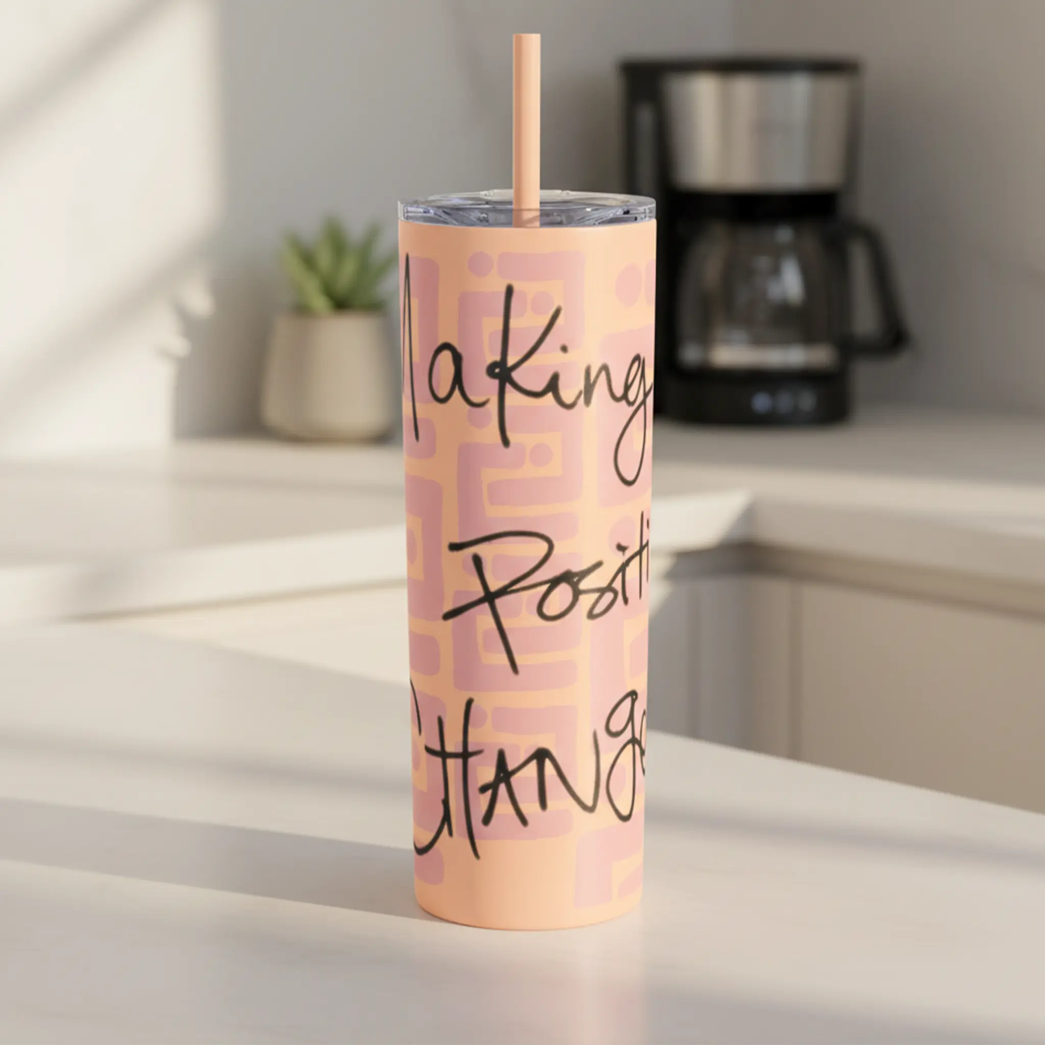 Freebrd Making Positive Changes peach blush skinny tumbler with black script text on a clean modern kitchen counter in soft natural morning light.
