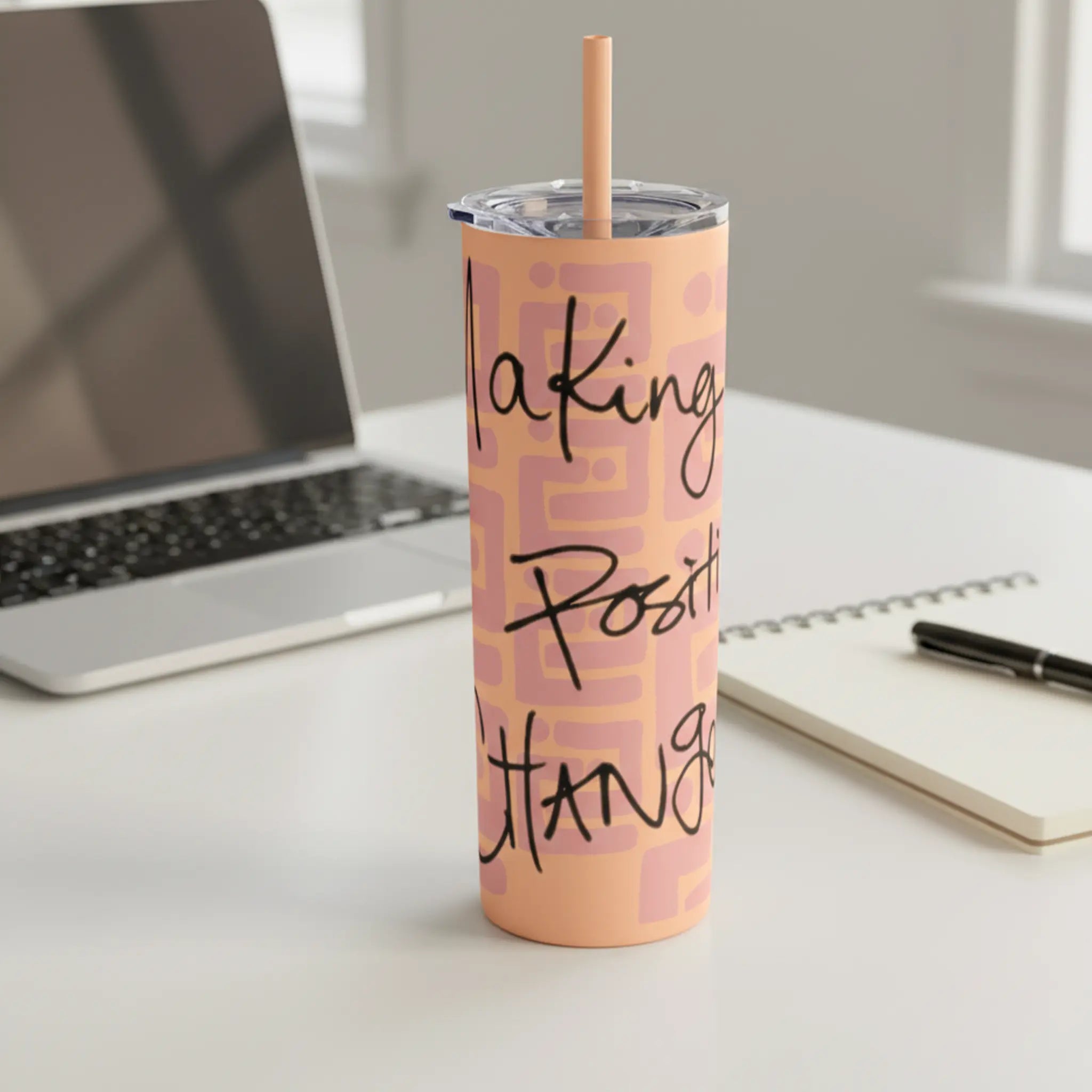 Freebrd Making Positive Changes 20oz peach blush skinny tumbler with black script text sitting on a clean modern work desk with soft natural light and laptop in background.