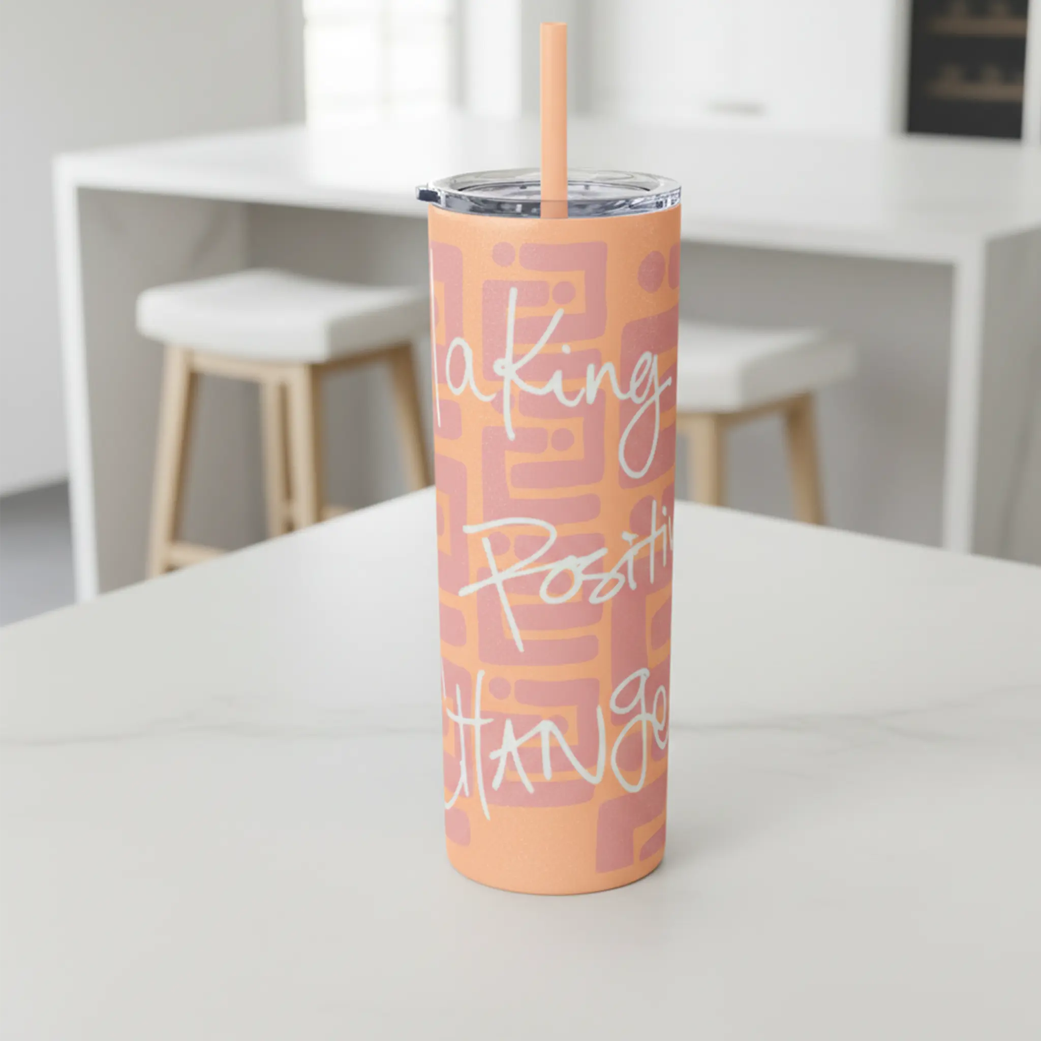 Freebrd Making Positive Changes peach blush skinny tumbler with white glitter script text on a bright white kitchen island in a clean airy kitchen setting.