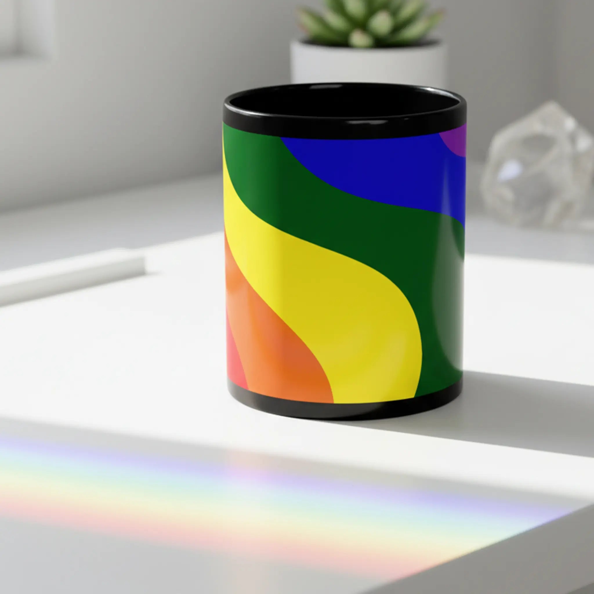 Freebrd Rainbow Wave black ceramic mug with bold full spectrum rainbow wave design sitting on a clean modern desk with colorful rainbow prism light streaks in a bright minimal setting.