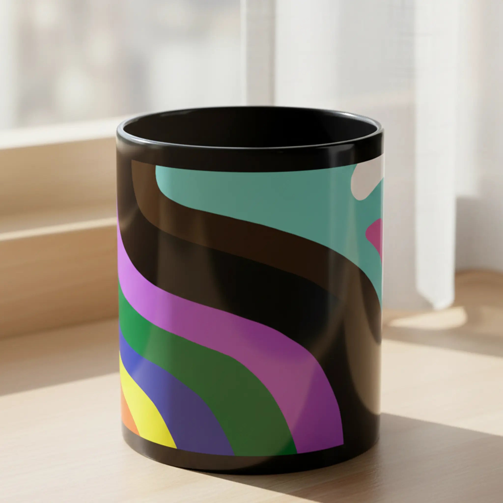 Freebrd Support Love black ceramic mug with bold flowing Progress Pride wave design in teal pink white brown black purple green blue yellow orange and red sitting on a warm wooden windowsill with soft natural light.