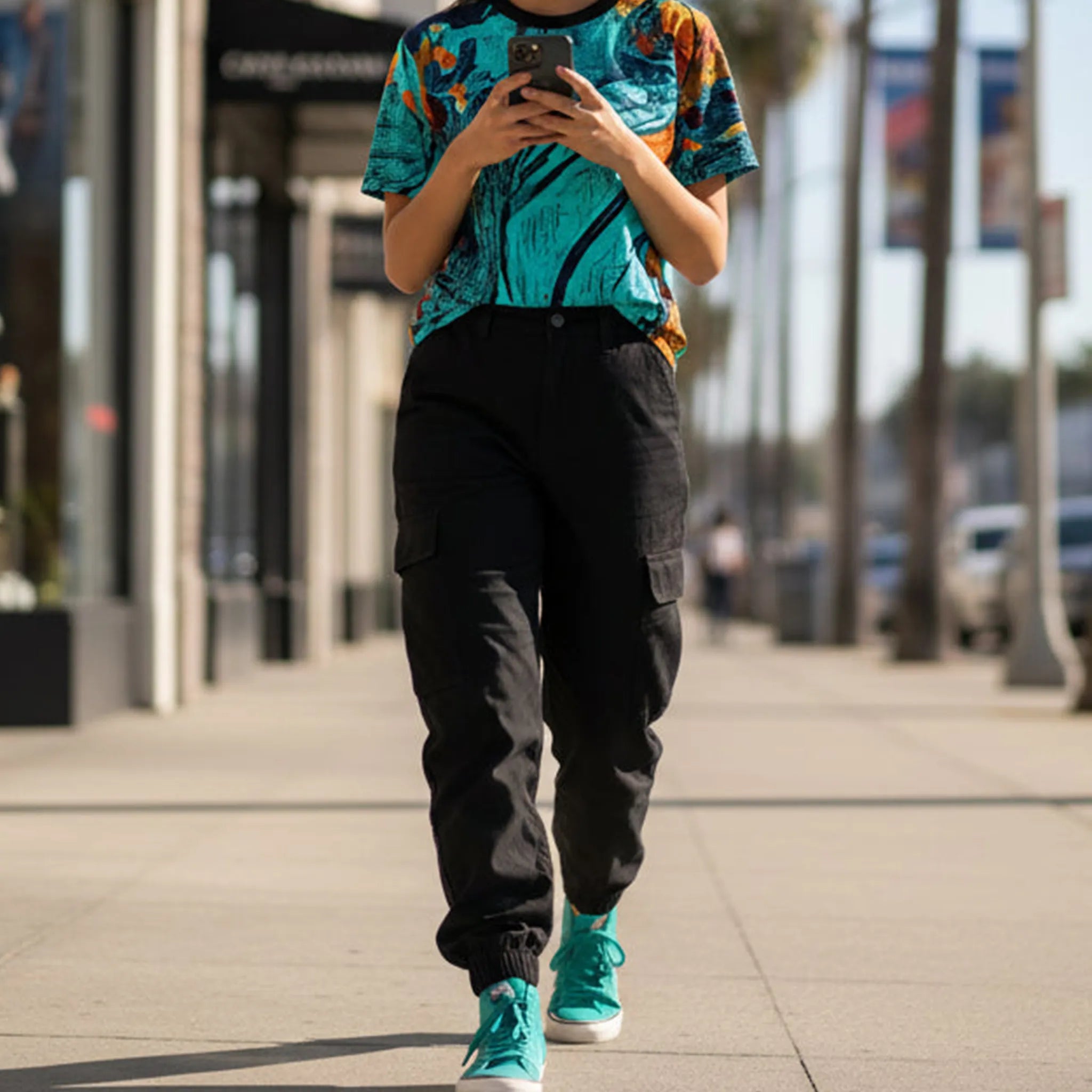 A front view of the Freebrd abstract all-over-print tee in teal and orange, styled with dark slim jeans and white sneakers on an urban street with natural light.
