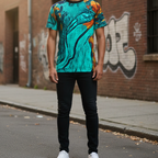 A front view of the Freebrd abstract all-over-print tee in teal and orange worn in an urban setting with a brick wall and graffiti backdrop.